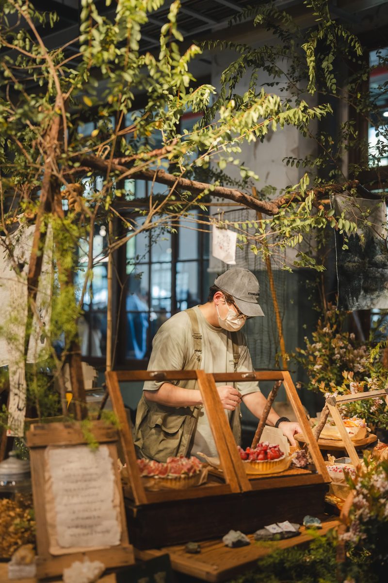緑の枝葉で飾られたブースで作品を並べる出店者